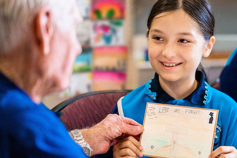 Student and a veteran looking at a postcard of honour. 